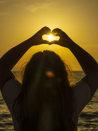 Portrait of woman with heart shape against sky during sunset
