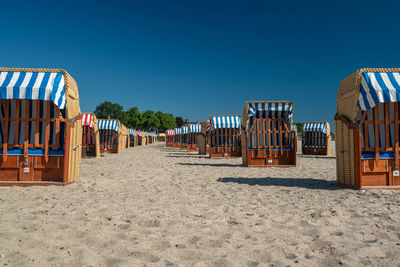 Hooded chairs on beach against clear blue sky