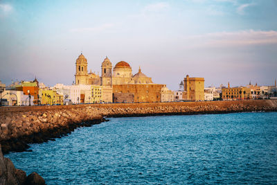 View of buildings by sea against sky in city