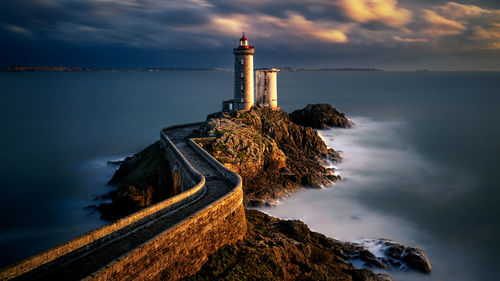 Tower by sea against sky during sunset