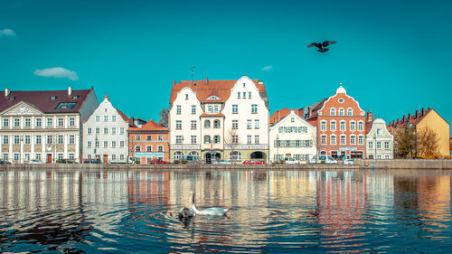 Buildings by river against clear blue sky