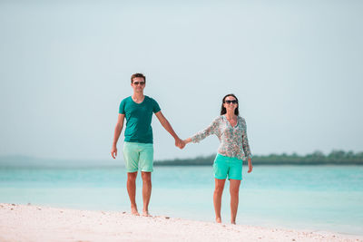 Full length of young couple standing on beach against sky