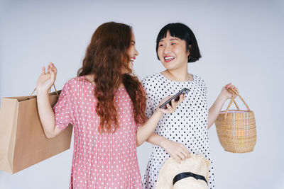 Lesbian couple using smart phone while holding bags against gray background