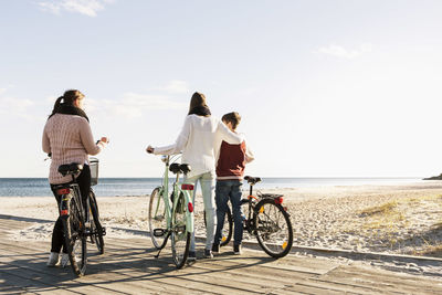 Full length of friends with bicycles on boardwalk at beach