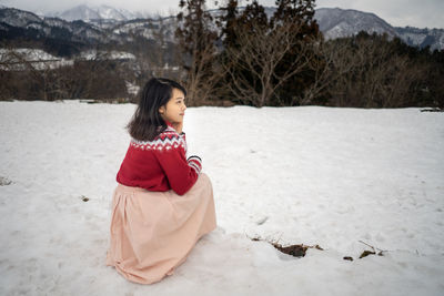 Girl crouching on snow covered land