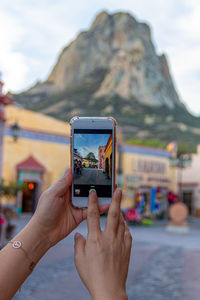 Midsection of person photographing with mobile phone against mountain