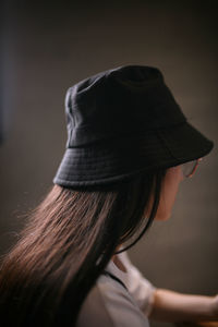 Close-up of woman wearing hat sitting against colored background