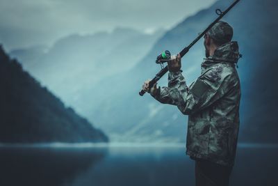 Side view of man fishing in lake against mountains