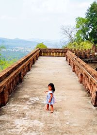 High angle portrait of girl walking on footpath against cloudy sky