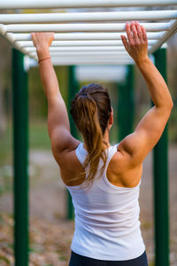 Rear view of woman exercising on monkey bars in park