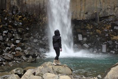 Rear view of man standing on rock looking at waterfall