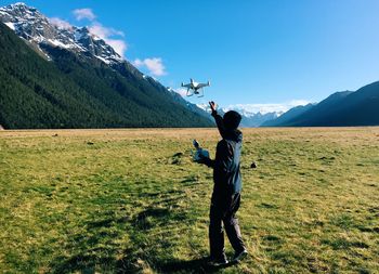 Man photographing woman standing on grass against sky