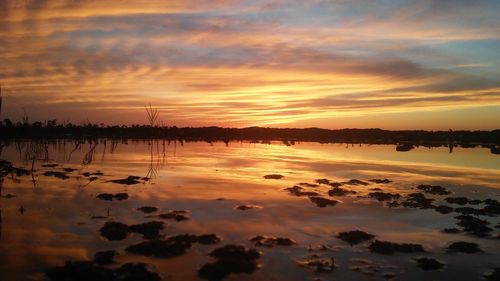 Scenic view of lake against cloudy sky during sunset