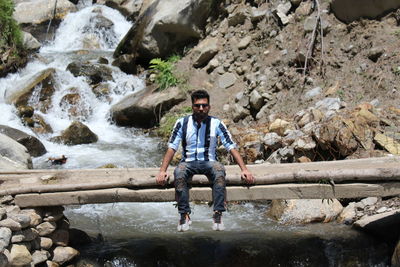 Full length of young man sitting over river on plank