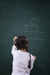 Rear view of girl solving mathematics on blackboard
