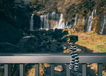Close-up of camera on railing against trees
