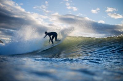 Silhouette man surfing in sea against sky