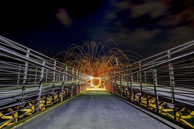 Light trails on footbridge against sky at night