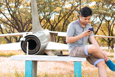 Full length of man using mobile phone while sitting on tree