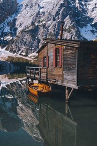 Boat moored by wooden cabin against snowcapped mountain