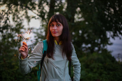 Portrait of young woman standing against trees