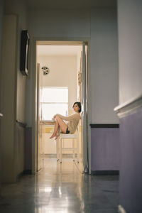 Side view portrait of young woman sitting on chair in kitchen