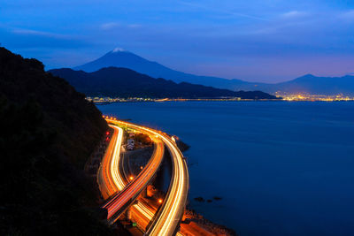 Light trails on road by mountain against sky at night