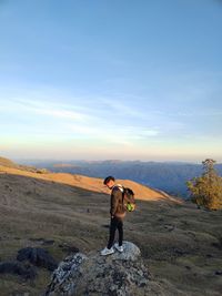 Rear view of man standing on field against sky during sunset