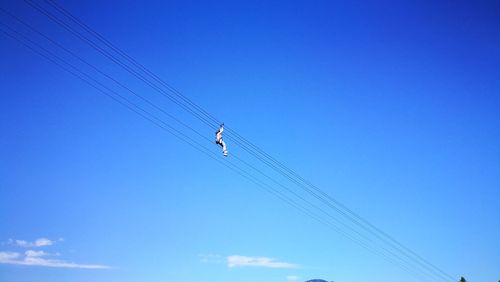 Low angle view of people flying against clear blue sky