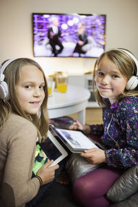 Portrait of smiling sisters listening music on digital tablets in living room