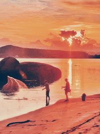 People standing on beach against sky during sunset