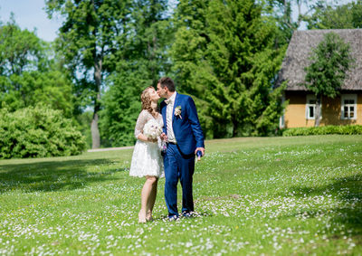 Full length of bride and bridegroom kissing at lawn on sunny day