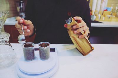 Midsection of person filling containers with roasted coffee beans in cafe