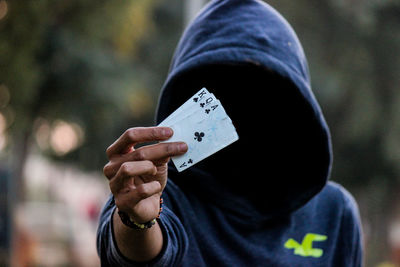 Man wearing hood while showing cards