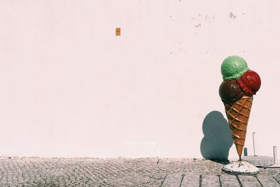 Ice cream cone sculpture on footpath against wall