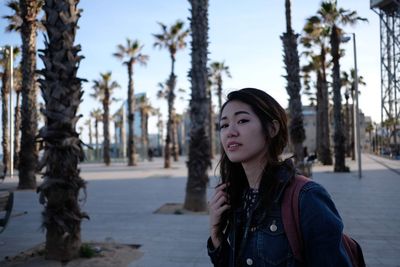 Portrait of young woman looking away by palm trees