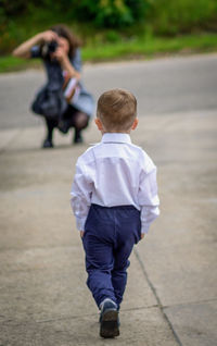 Rear view of photographer, photographing little boy walking on city