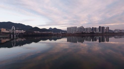 Reflection of city on lake against sky during sunset