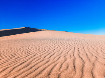 Sand dunes in desert against clear blue sky