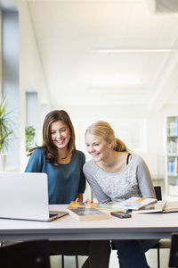 Smiling teenage girls using laptop at table in school library