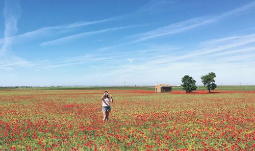 Woman standing amidst plants in field against sky on sunny day