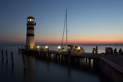 Lighthouse by lake against sky during sunset