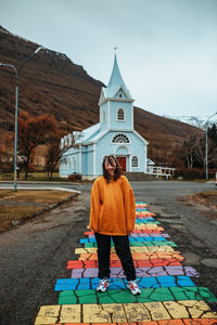 Young happy tourist happy on street between buildings of village near cathedral and mountain
