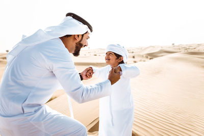 Smiling father and son enjoying while standing in desert