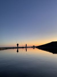 Silhouette people fishing in lake against sky during sunset