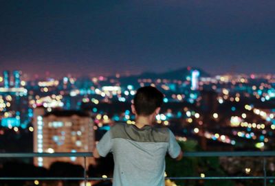 Rear view of man looking at illuminated cityscape against sky