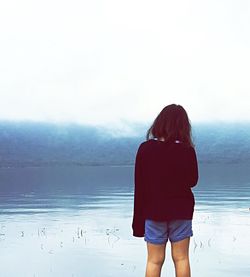 Rear view of woman standing on beach against clear sky