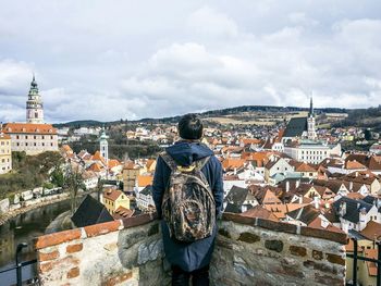 Rear view of man with backpack looking at cesky krumlov against cloudy sky