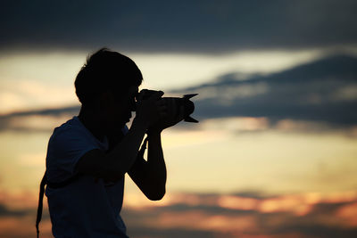 Side view of person photographing against sky during sunset