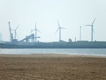 Windmills on beach against sky